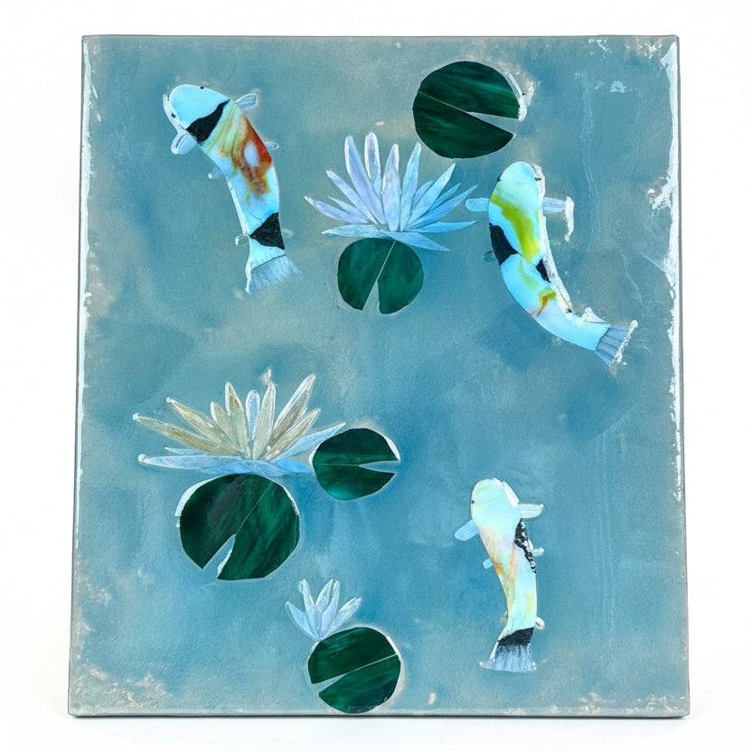 A square decorative mosaic featuring glass koi fish and water lilies on a textured light blue background, photographed against a plain white backdrop.