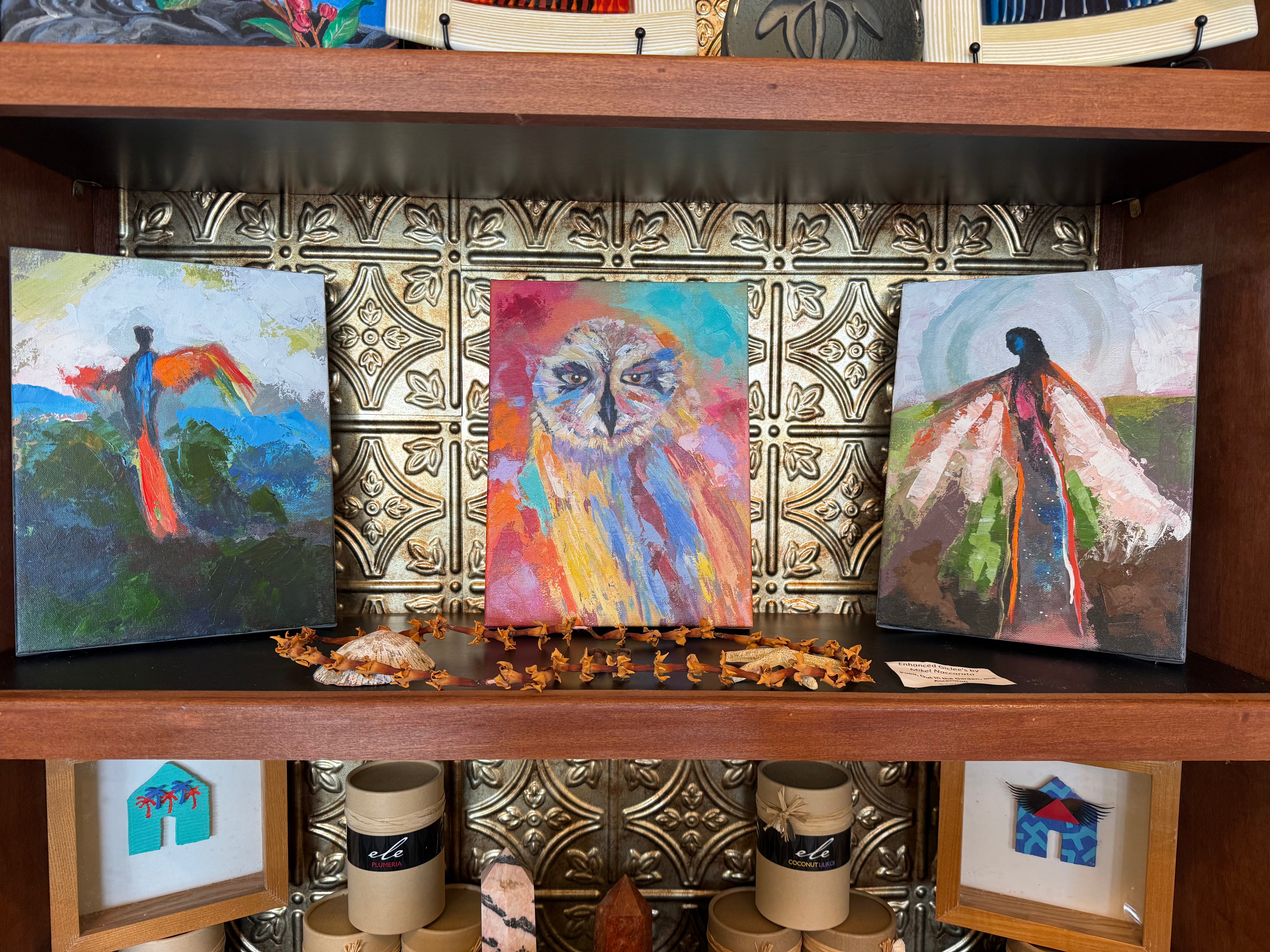 Three colorful paintings on a wooden shelf with decorative tiles.