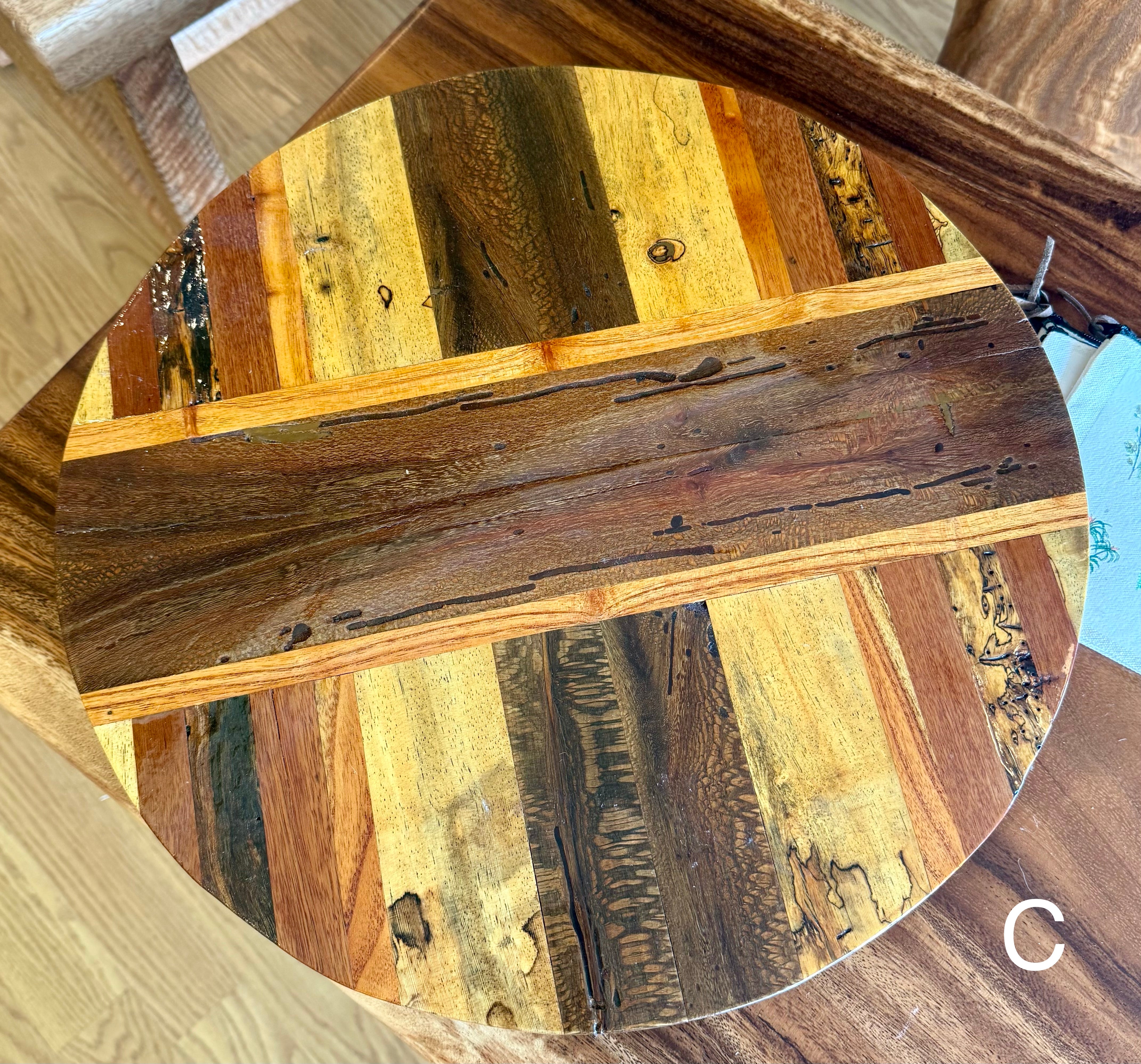 A circular wooden tabletop or tray top featuring a rustic patchwork design of natural wood planks in warm brown, tan, and golden tones, shown in a close-up view. lazy susan, hawaii wood