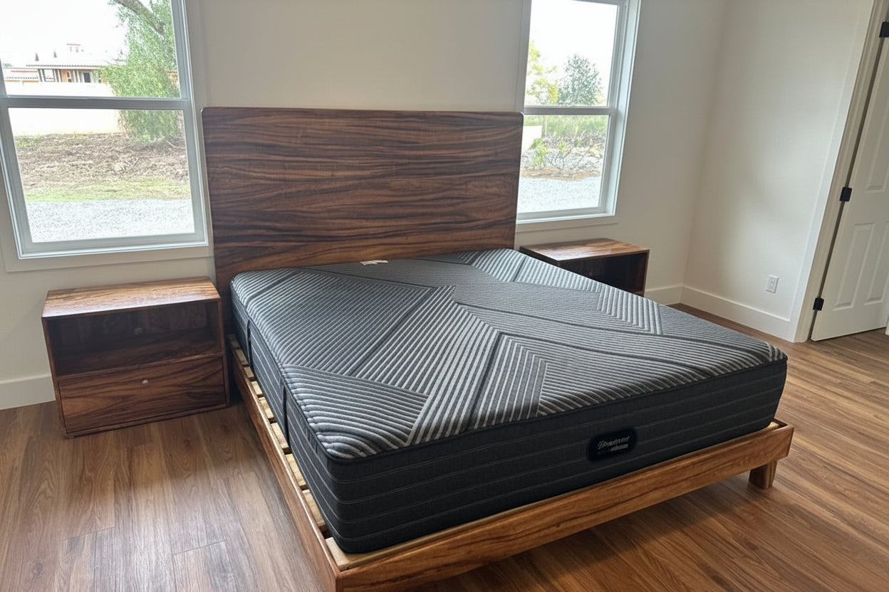 Wooden bed frame with mattress and bedding in a room with windows and a nightstand. custom hardwood bed frame hawaiian hardwoods monkeypod bed