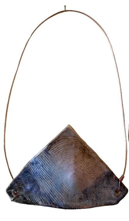 A handmade triangular wall vase and art piece with a textured, grey and blue center and thin copper wire loops for hanging, displayed on a textured beige wall next to other art pieces.