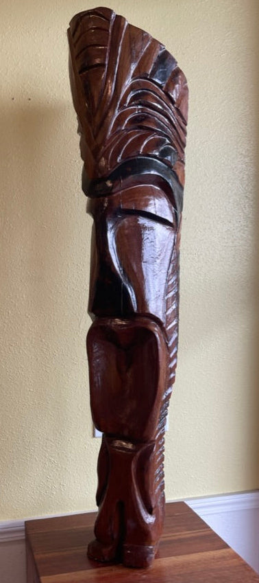 Carved wooden sculpture on a pedestal against a yellow wall hawaii tiki god