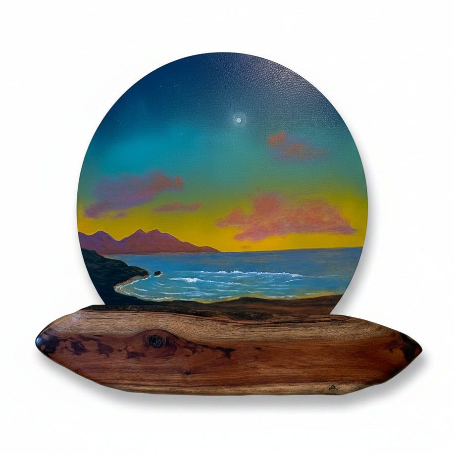 A circular landscape wall art piece mounted on a natural wood base, showing a sunset seascape with blue sky, yellow horizon, purple clouds, and mountains over water, displayed on a beige wall.