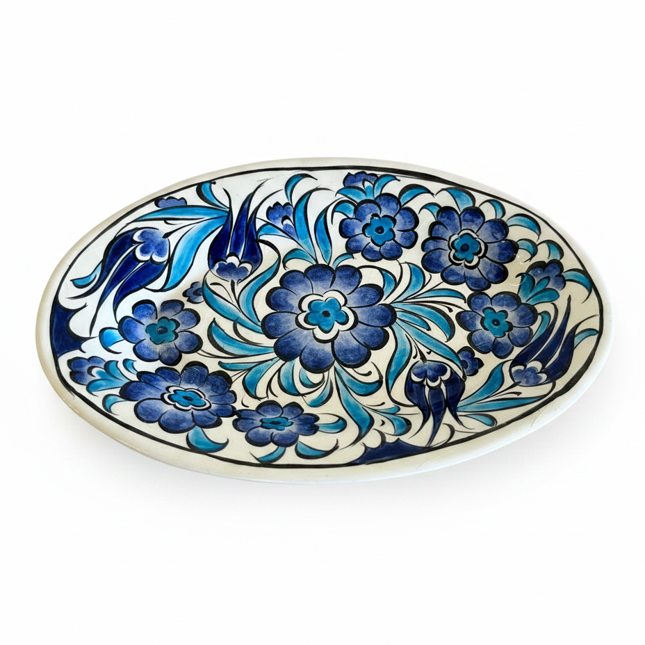 An oval ceramic serving platter with a hand-painted floral pattern in shades of blue and navy on a white background, shown on a wooden surface with a ruler for scale.