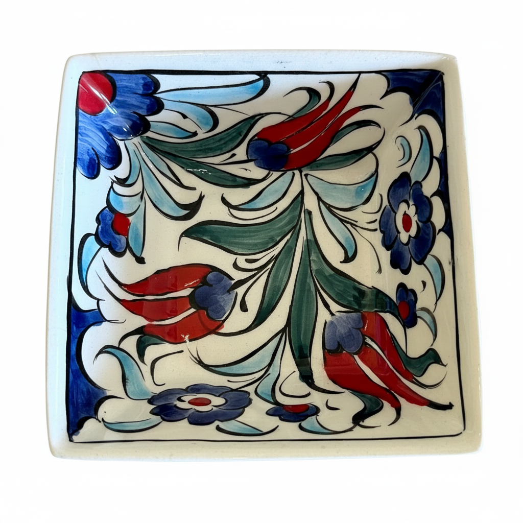 A square white ceramic plate with a hand-painted floral pattern in blue, red, and green, shown on a wooden surface with a measuring tape ruler at the bottom.