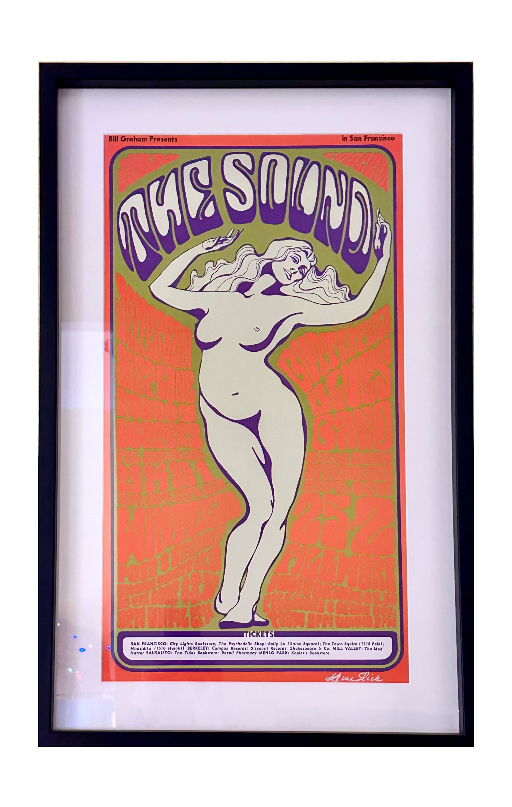 A framed art print featuring a retro-style poster with the text 'THE SOUND' and a stylized nude figure, mounted on a beige wall.