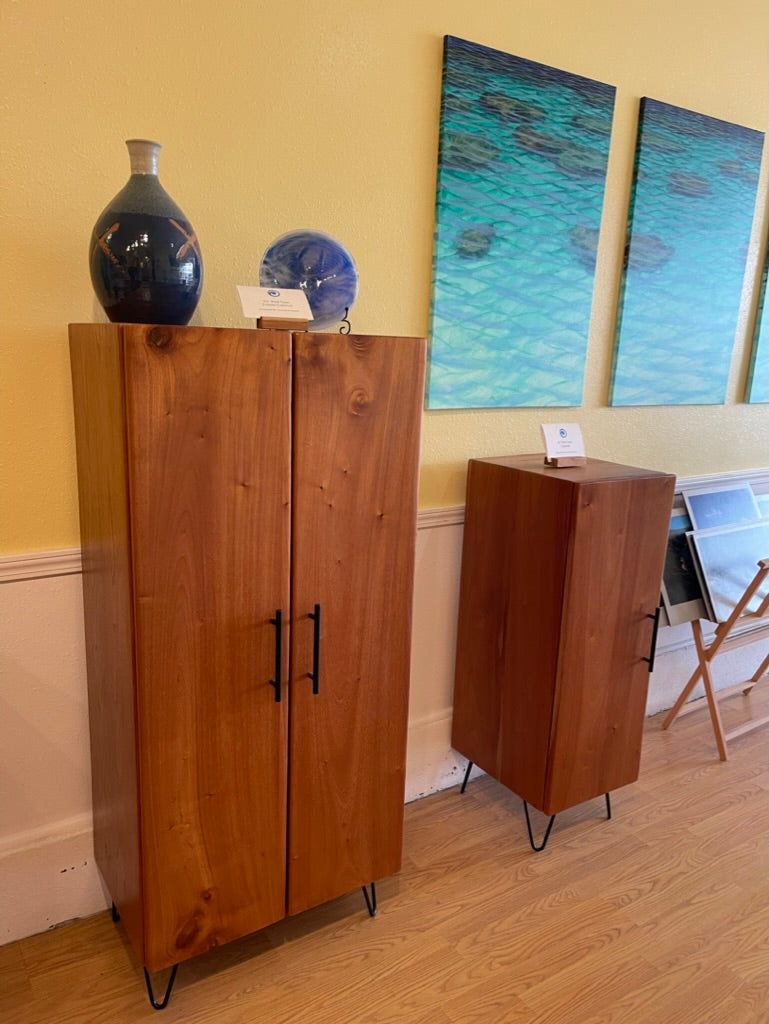 Wooden cabinet with a vase and decorative items on top, against a wall with abstract art.