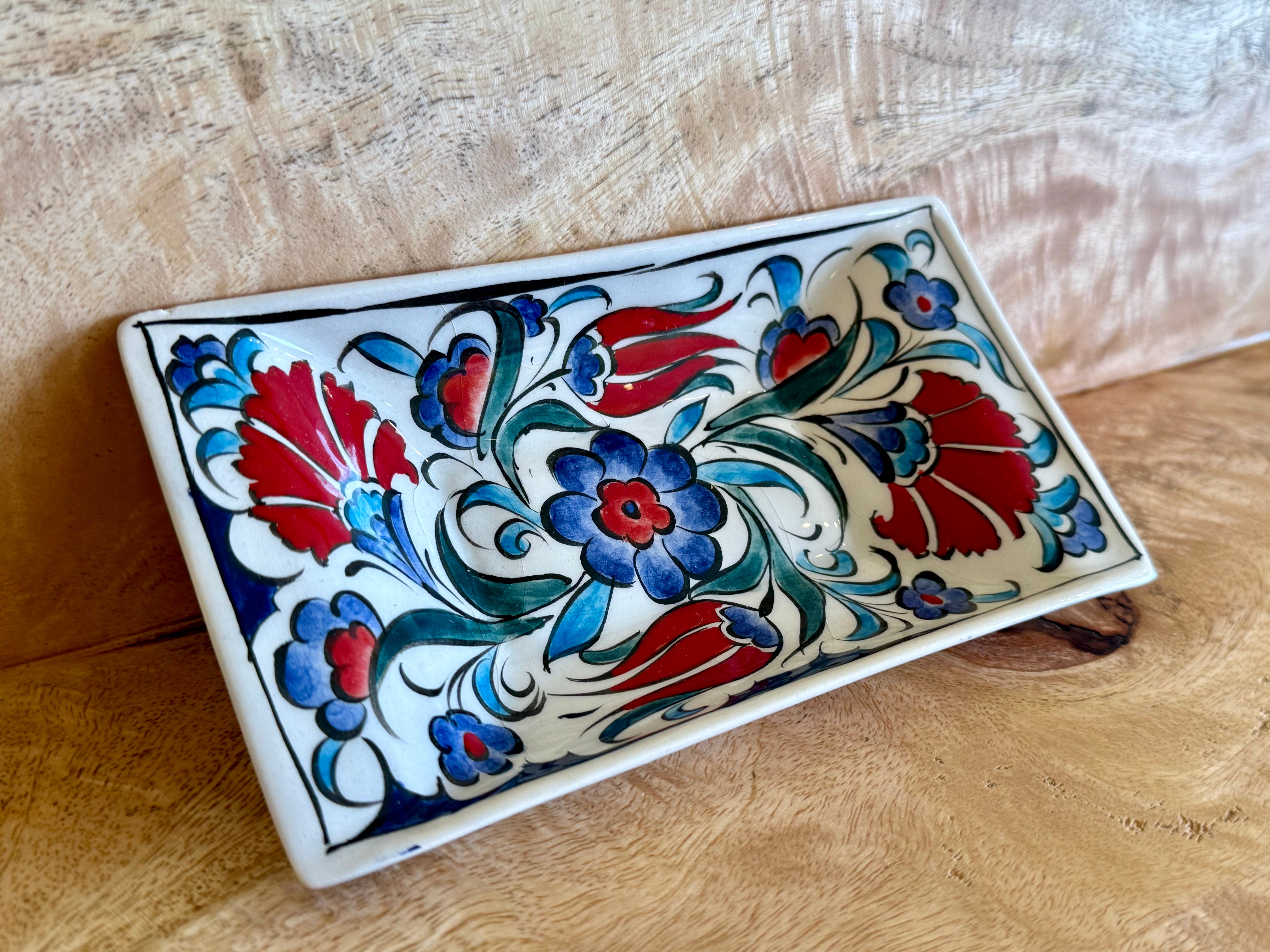 A rectangular ceramic serving tray with a hand-painted floral pattern in red, blue, and green on an off-white background, resting on a wooden surface.