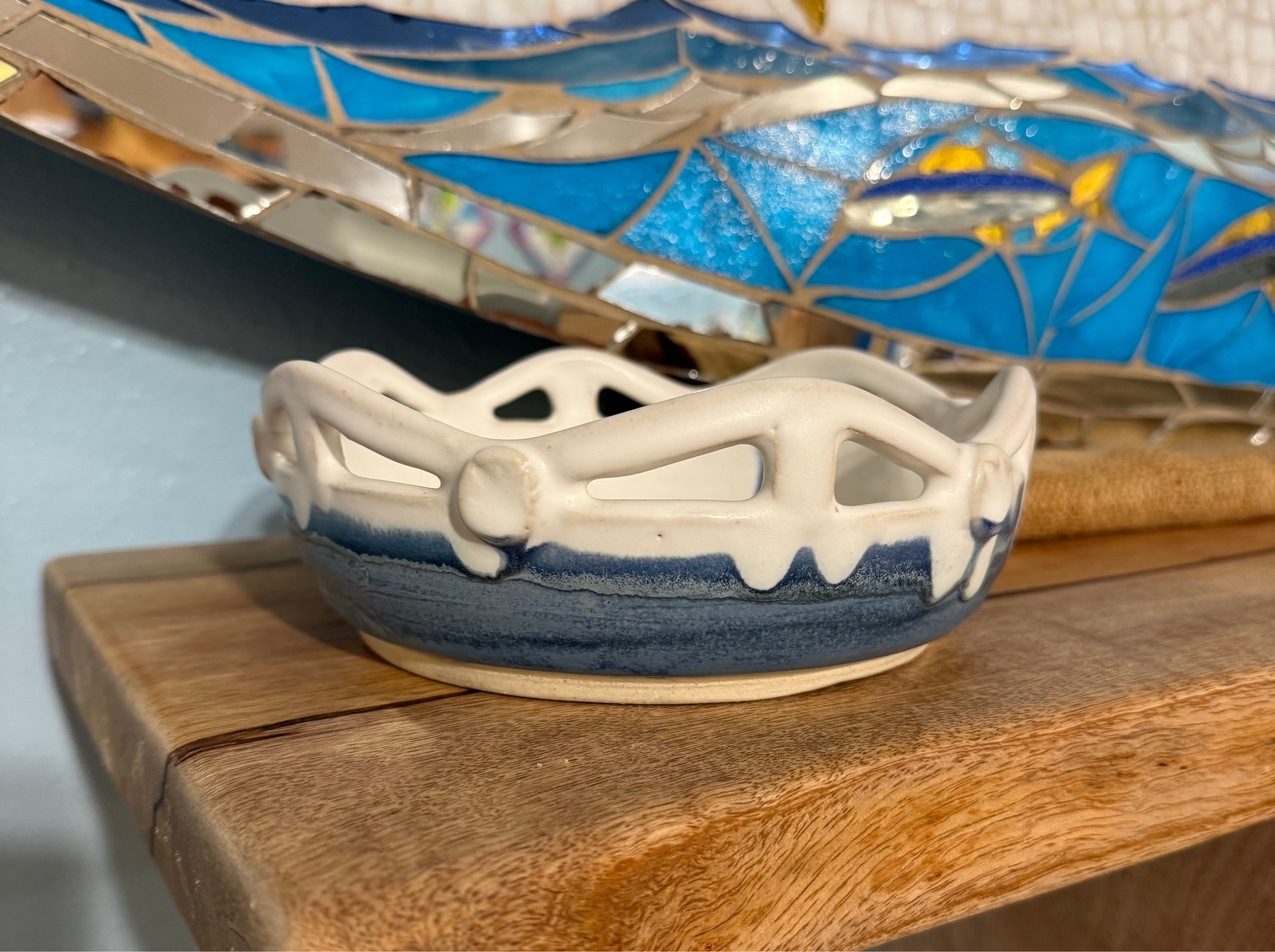Decorative ceramic dish with blue and white design on a wooden shelf.