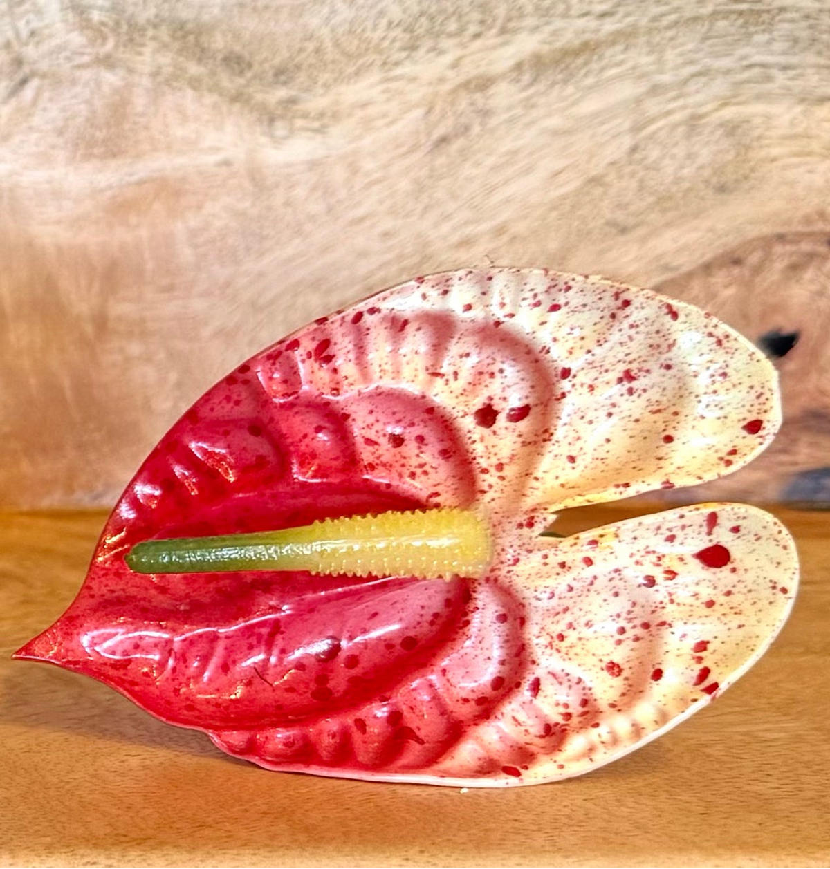 Four decorative ceramic flowers arranged on a wooden surface against a textured wood background. The set includes a white orchid with a red center, a red and yellow marbled flower, a green and yellow orchid, and a red and cream anthurium.