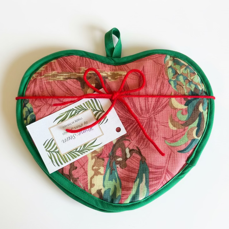 Heart-shaped pot holder with floral pattern and red string, on a wooden surface.