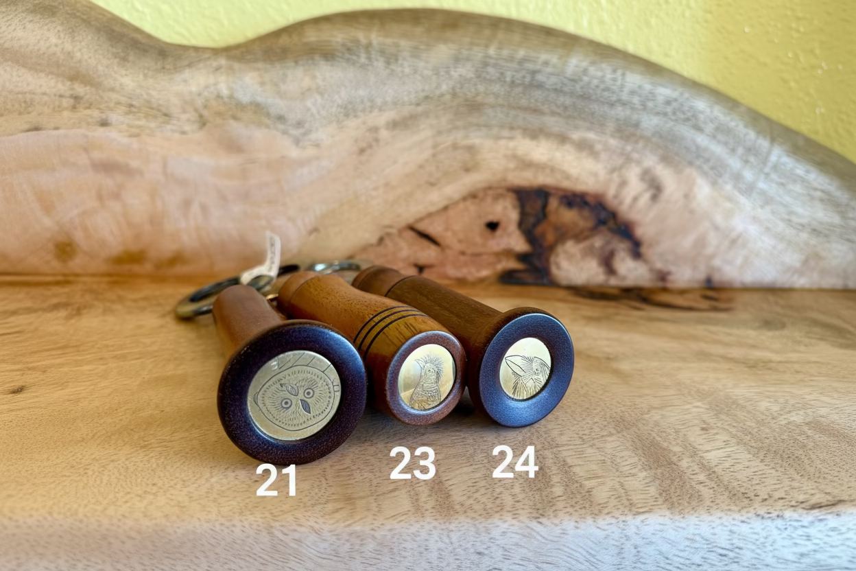 Three wooden bottle openers with polished dark brown handles and circular brass medallion ends, displayed on a wooden surface in front of a natural wood slab background.