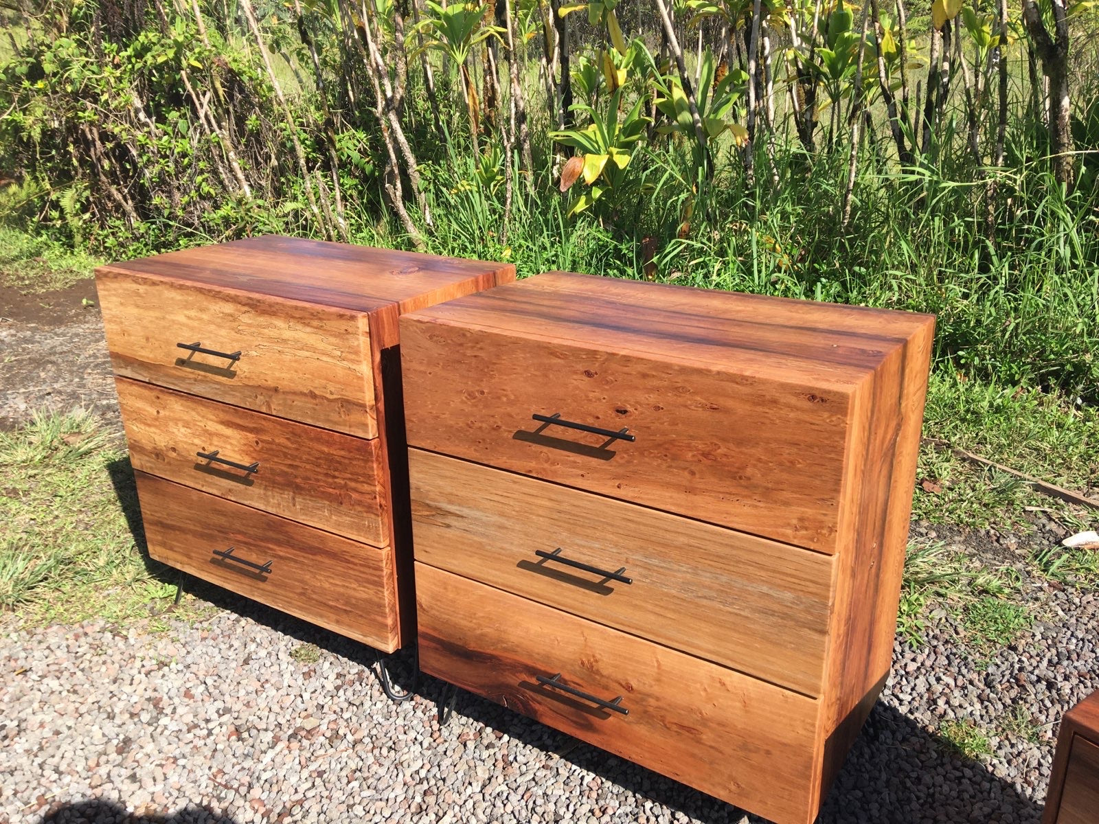 Two wooden dressers outdoors on a gravel surface with greenery in the background
