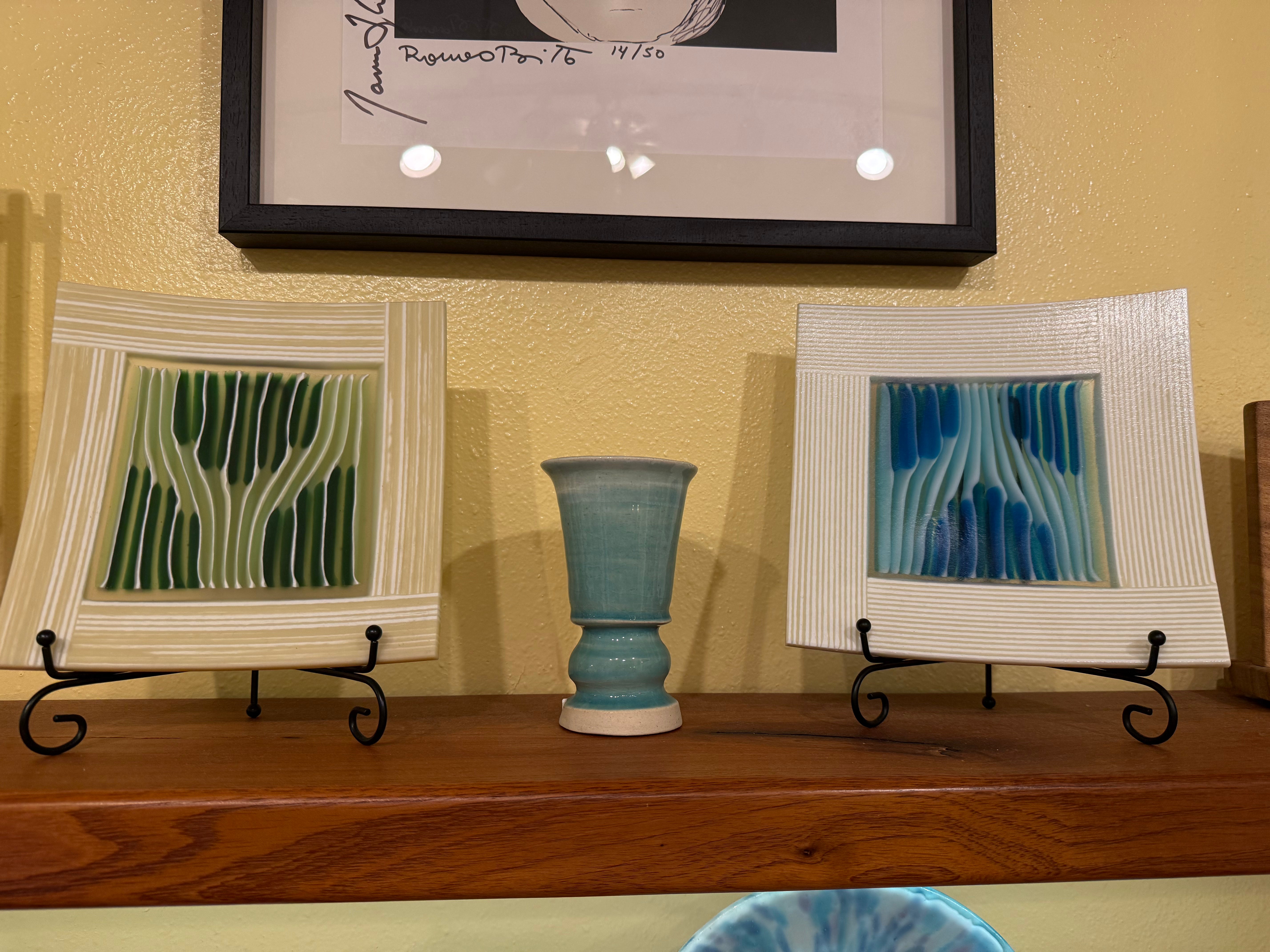 Two framed artworks and a blue vase on a wooden surface with a yellow wall in the background.