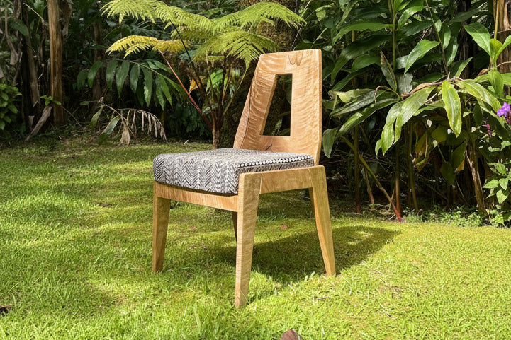 Wooden chair with a patterned cushion on grass with greenery in the background