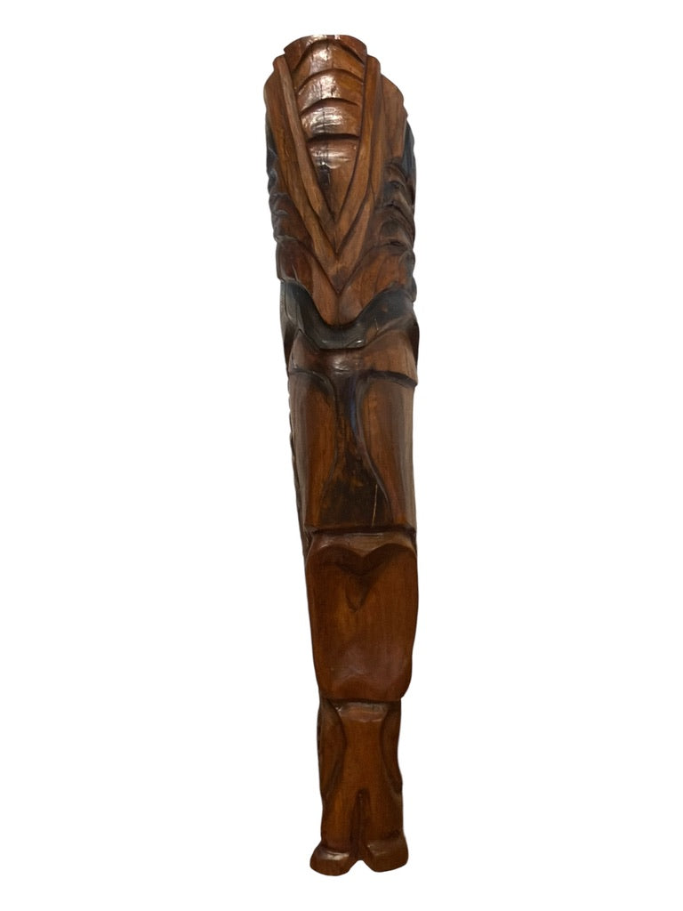 A carved wooden wall plaque or sculpture featuring a stylized face with deep carved details, shown vertically against a plain white background.
