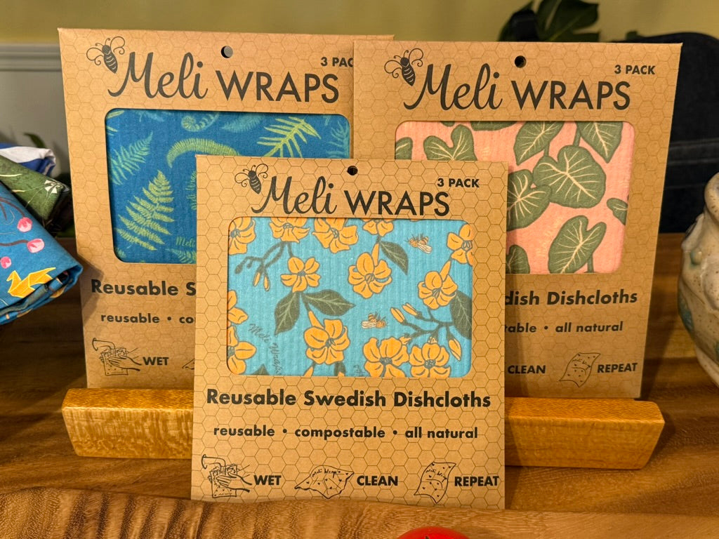 Three packages of Meli Wraps reusable Swedish dishcloths on a wooden surface.